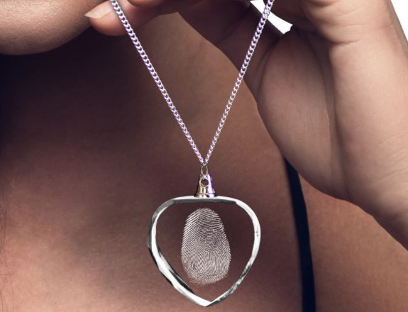 A woman holds a heart-shaped necklace engraved with her husband’s fingerprint.