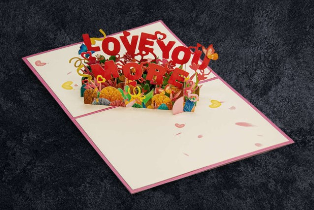 A romantic pop-up anniversary card that says, “Love You More.”